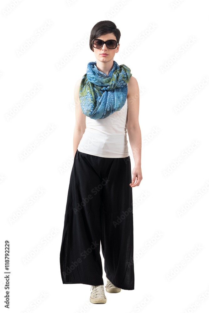 Fototapeta premium Gorgeous runway fashion model with sunglasses walking and looking at camera. Full body length portrait isolated over white studio background.