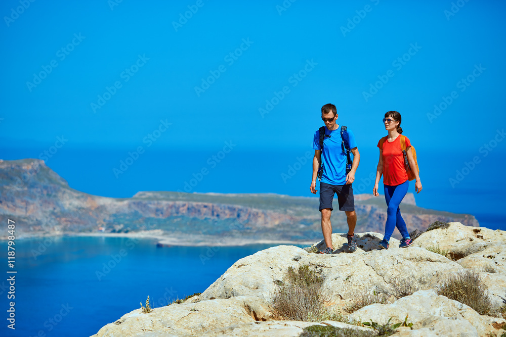 couple of travelers with backpack standing on the cliff against sea and blue sky at early morning