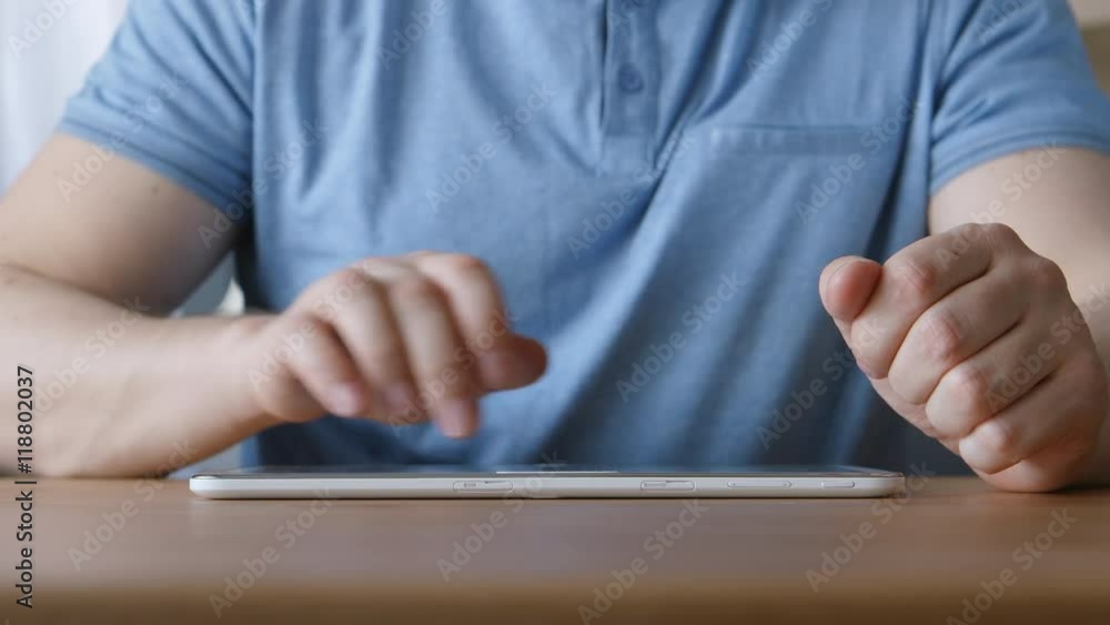 A hands of young man touching on a tablet PC at the table at home A hands of young man touching on a tablet PC at the table at home