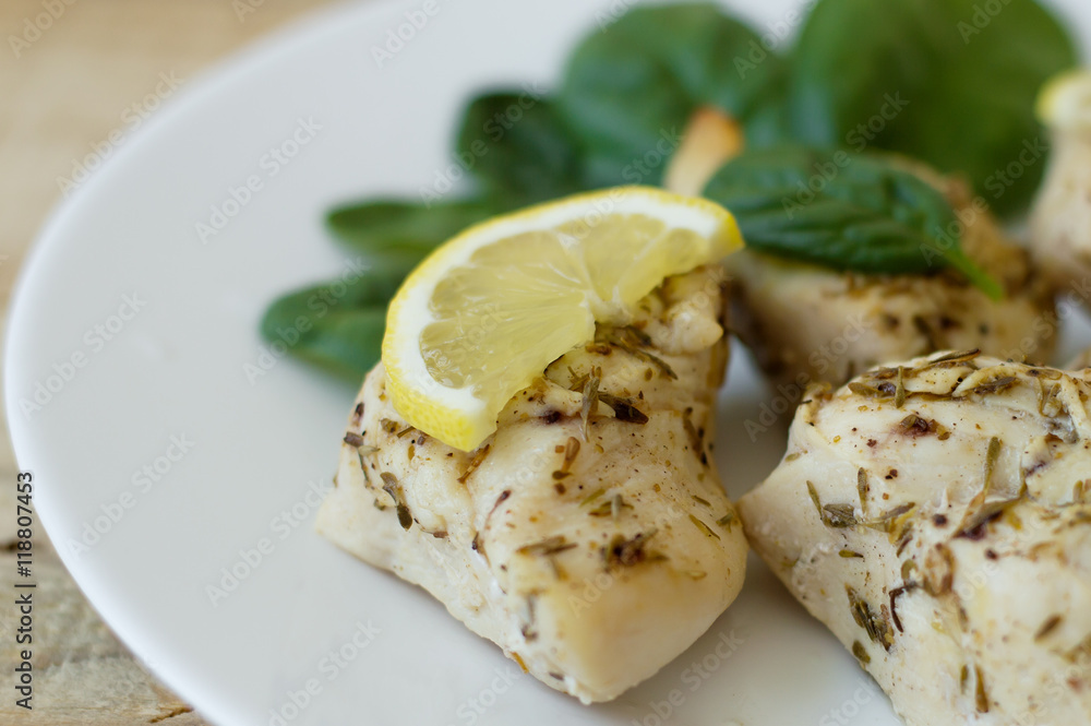 Chopped chicken fillet baked with thyme and served with fresh lemon slice and small spinach leaves