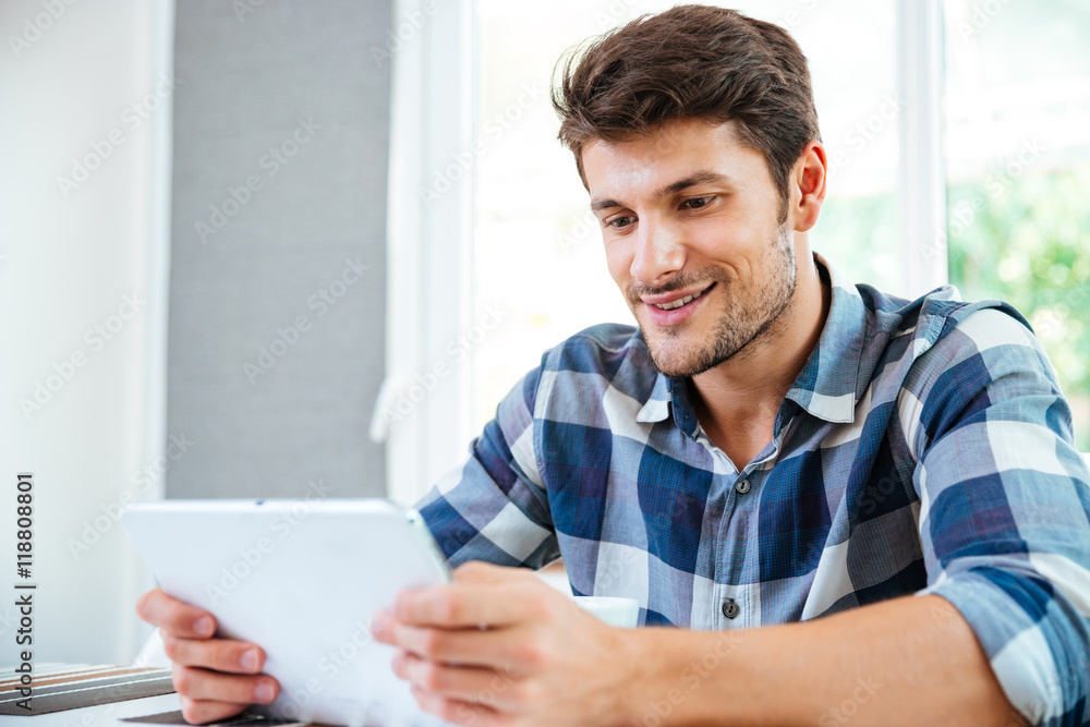 Smiling young man sitting and using tablet at home Smiling young man sitting and using tablet at home