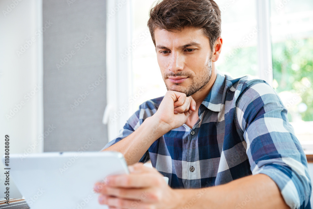 Pensive young man thinking and using tablet at home Pensive young man thinking and using tablet at home