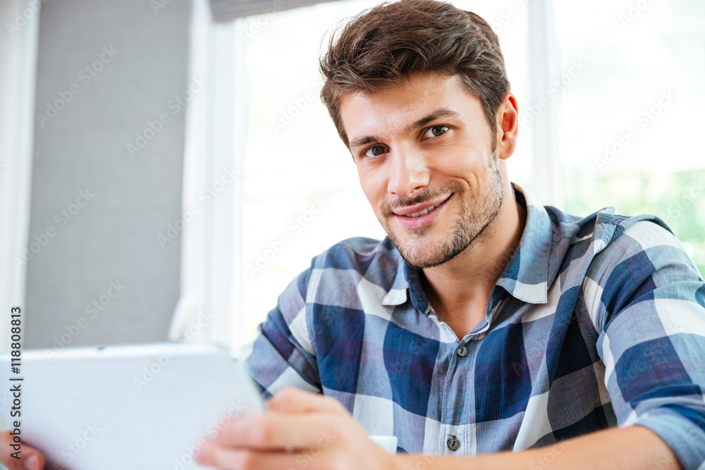 Happy young man in checkered shirt using tablet at home Happy young man in checkered shirt using tablet at home