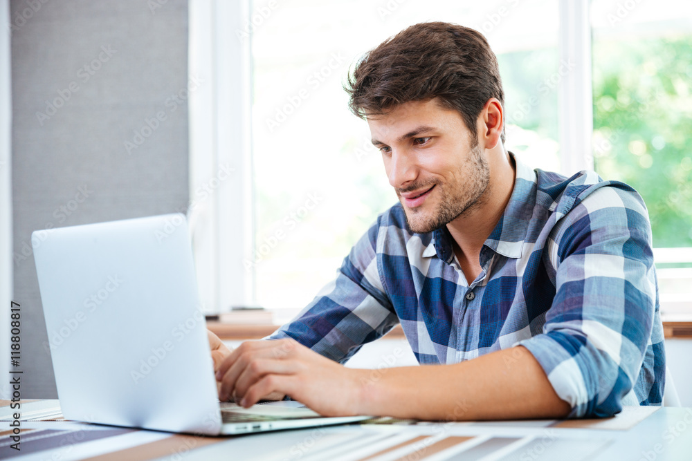 Man in plaid shirt sitting and using laptop at home Man in plaid shirt sitting and using laptop at home