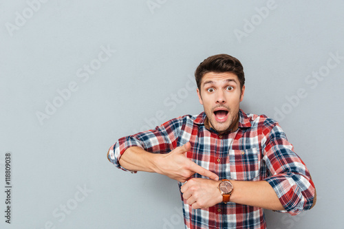 Фотография Amazed young man in plaid shirt pointing on wristwatch