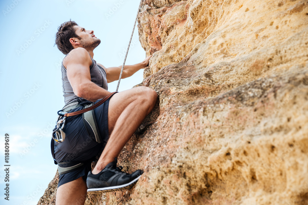 Young man climbing a steep wall in mountain