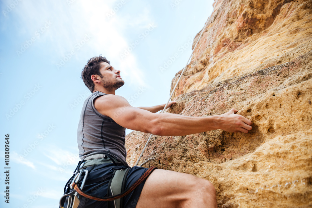 Young sportsman climbing up a rock cliff