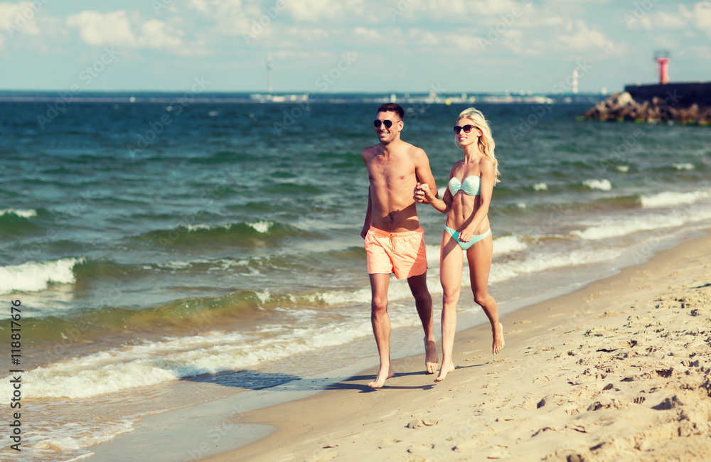 happy couple in swimwear running on summer beach