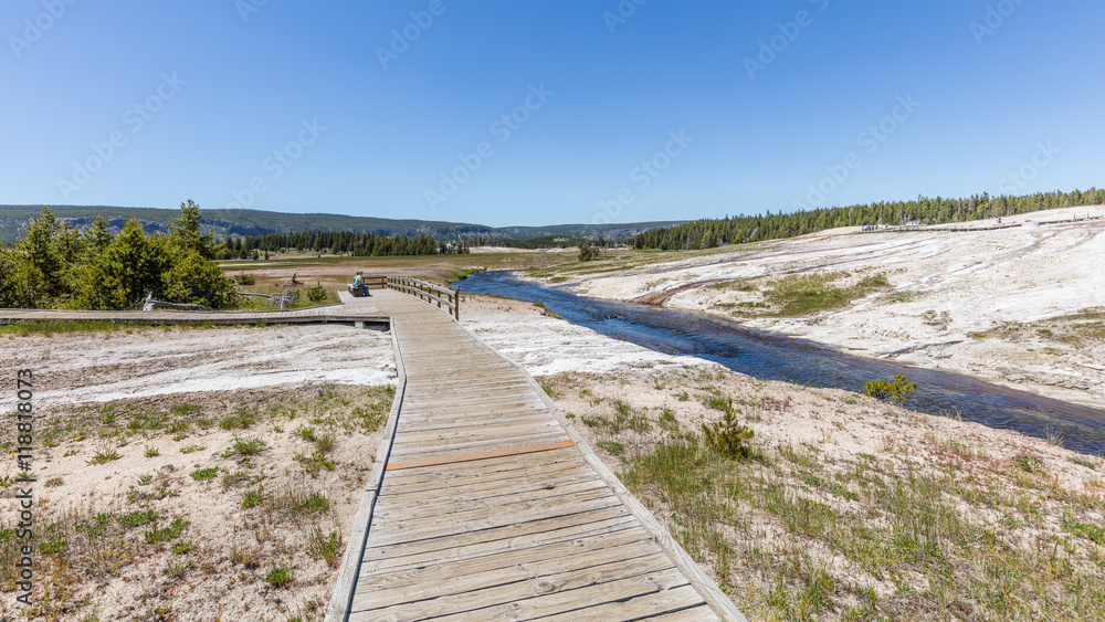 Fototapeta premium Colorful landscapes of geothermal activity. Wooden walkway among the geysers. Old Faithful Geyser, Yellowstone National Park, Wyoming, USA