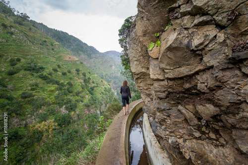 Woman walking at footpath along the rocky cliffs. Levada Nova hike, Madeira island.