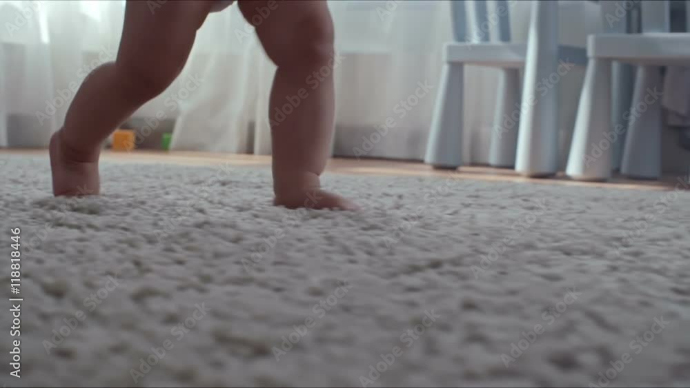Closeup of barefoot legs of little child learning how to step on the carpet with help of mother Closeup of barefoot legs of little child learning how to step on the carpet with help of mother