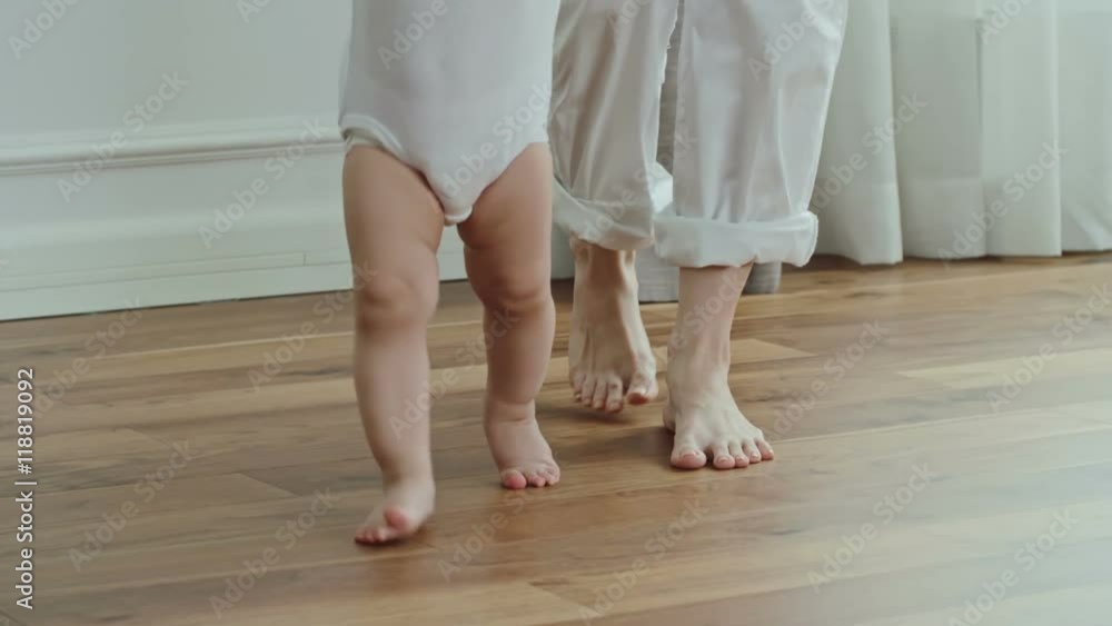 Adorable happy baby smiling while making first steps with assistance of mother Adorable happy baby smiling while making first steps with assistance of mother