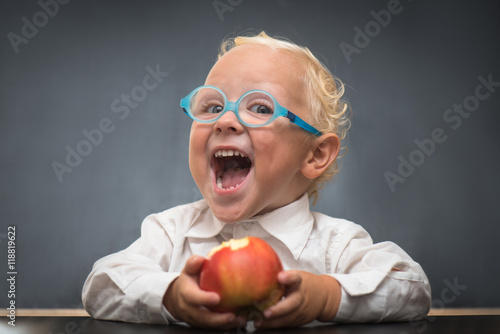 Cheerful baby on a gray background with a white shirt eating an