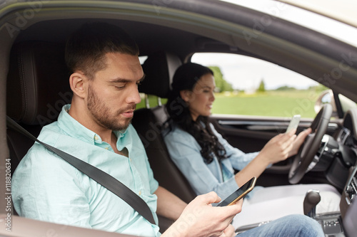 man and woman with smartphones driving in car