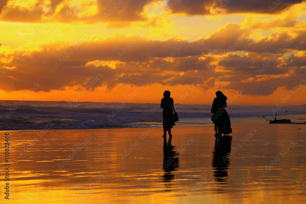 Two women walking along the ocean shore during sunset