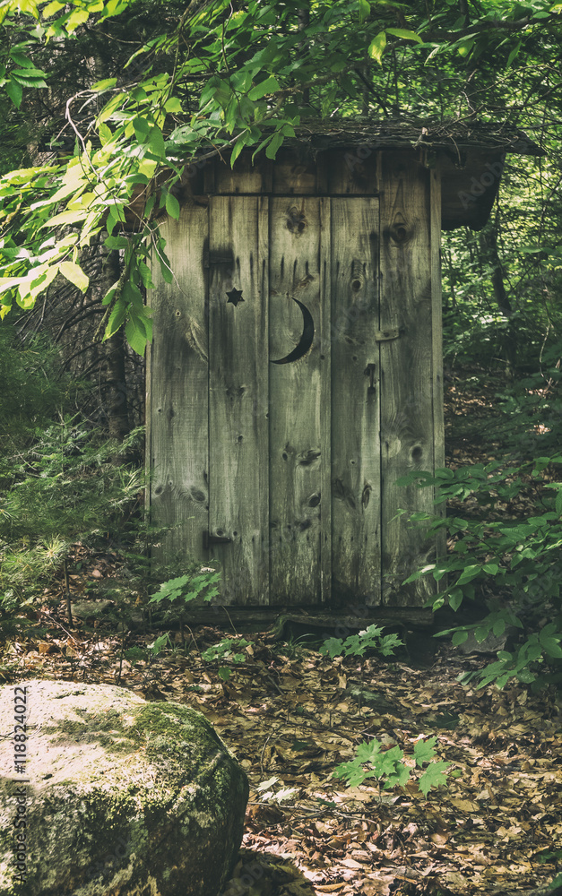 Classic Rural Outhouse. A typical old fashioned outhouse bathroom with a cut out moon on the door, in a wooded, forest area. Classic Rural Outhouse. A typical old fashioned outhouse bathroom with a cut out moon on the door, in a wooded, forest area.