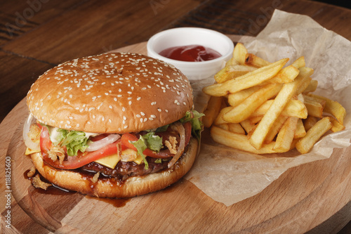 Cheeseburger with french fries and sauce on a brown wooden background