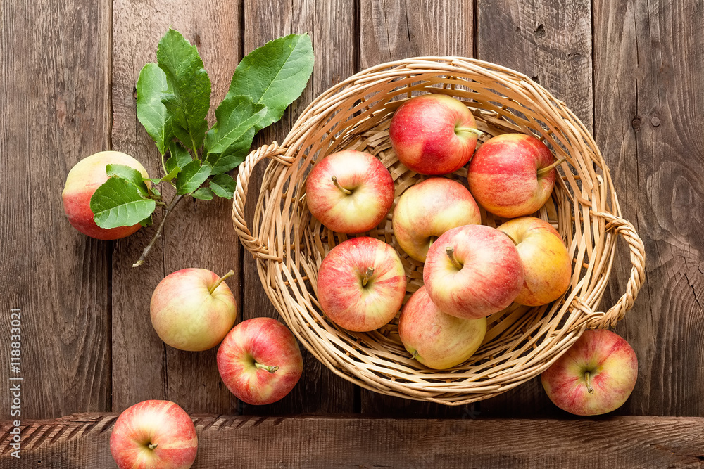 Fresh red apples in wicker basket on wooden table.