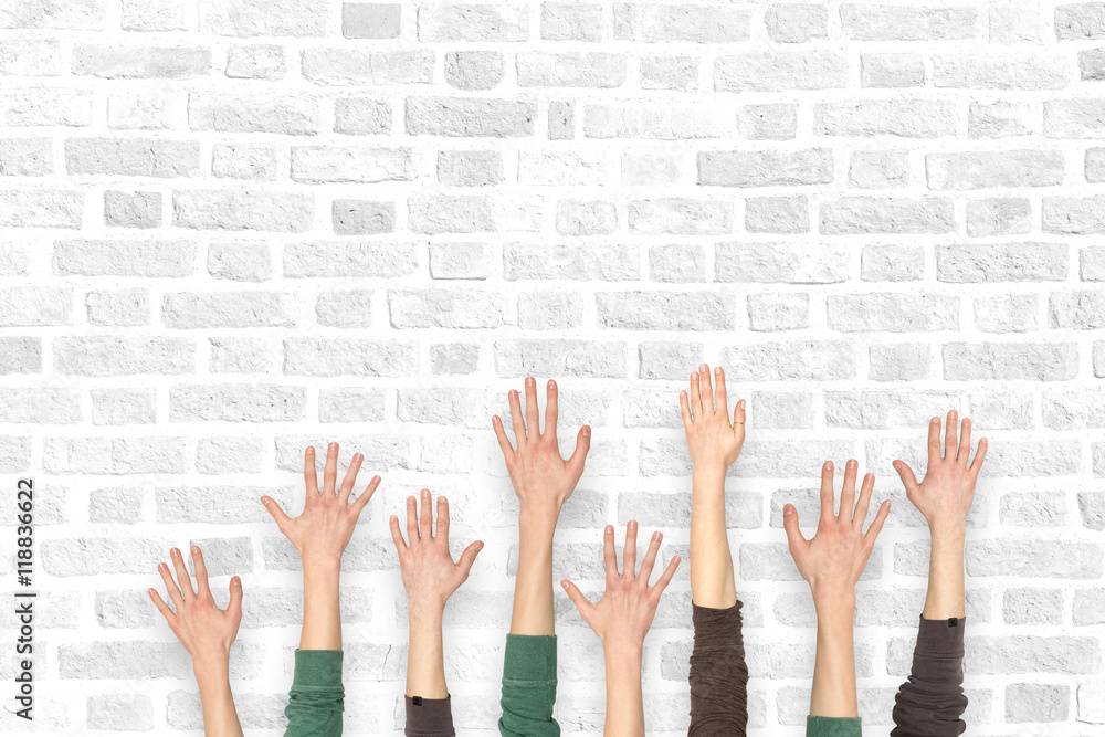 Many hands up on the background of a brick wall