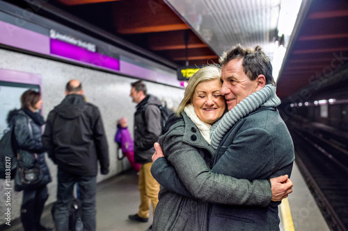 Senior couple standing at the underground platform, hugging, wai