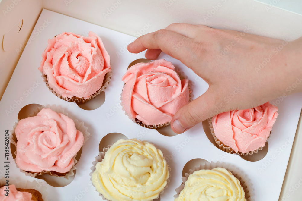 Cupcakes with pink and yellow cream in paper box on brown backgr Cupcakes with pink and yellow cream in paper box on brown backgr