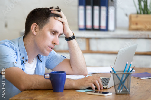 Εκτύπωση καμβά Portrait of young man sitting at the table in front of laptop, sleepy, tired, overworked or lazy to work