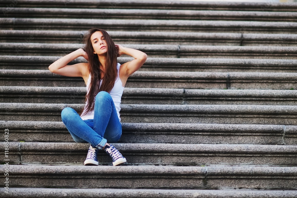 student brunette in white shirt and jeans sitting on stairs and looking up student brunette in white shirt and jeans sitting on stairs and looking up