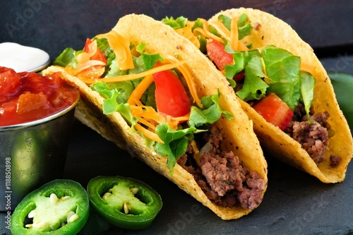 Hard shelled tacos with ground beef, lettuce, tomatoes and cheese close up, on slate background