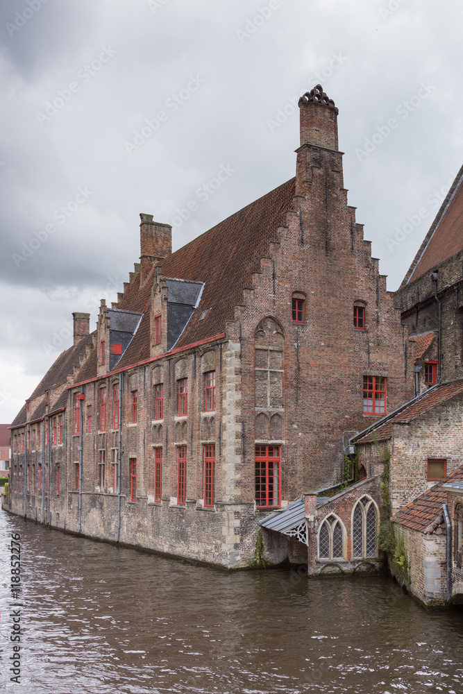 Brugge, Belgium - August 10, 2016: Medieval Sint Jans Hospital building along canal in Bruges. Rainy skies and dark canal water.