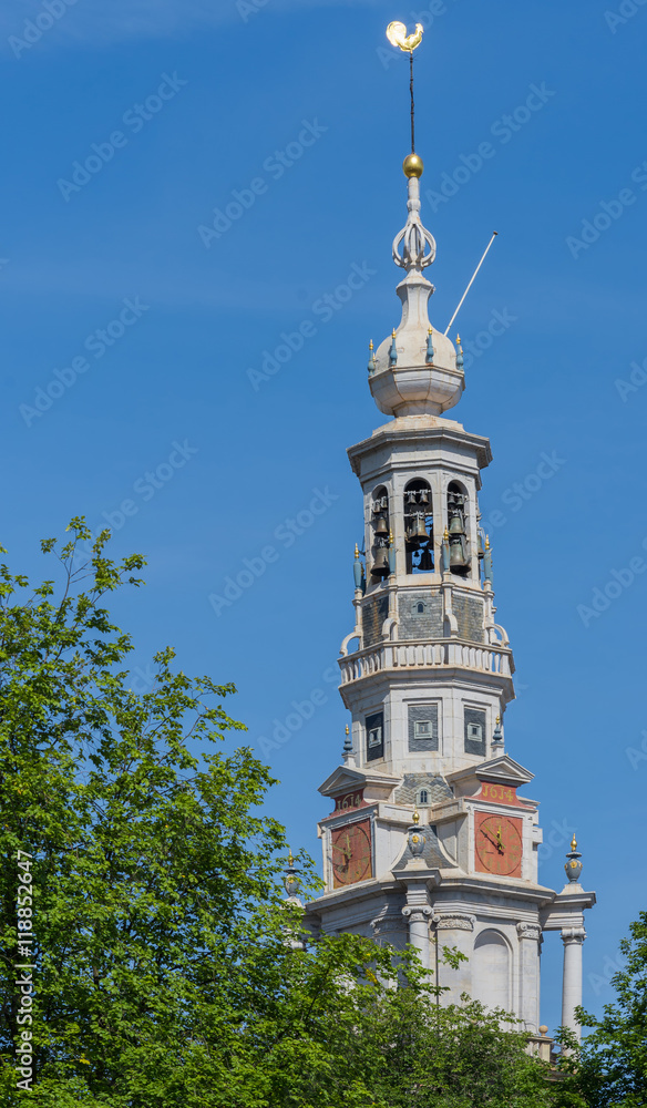 Amsterdam, the Netherlands - August 16, 2016: The spire of the Zuiderkerk against blue sky with green tree in lower left corner.