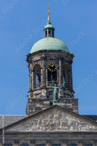 Amsterdam, the Netherlands - August 16, 2016: The top of the Royal Palace on the Dam against blue sky. Cut off at triangle mural. Statue, niche and clock.