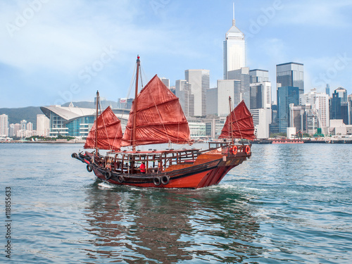 Murais de parede Hong Kong traditional red-sail Junk boat on city skyscrapers background