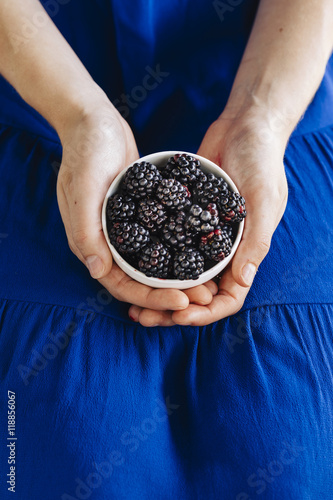 Young woman in blue dress holding a white bowl containing blackberries