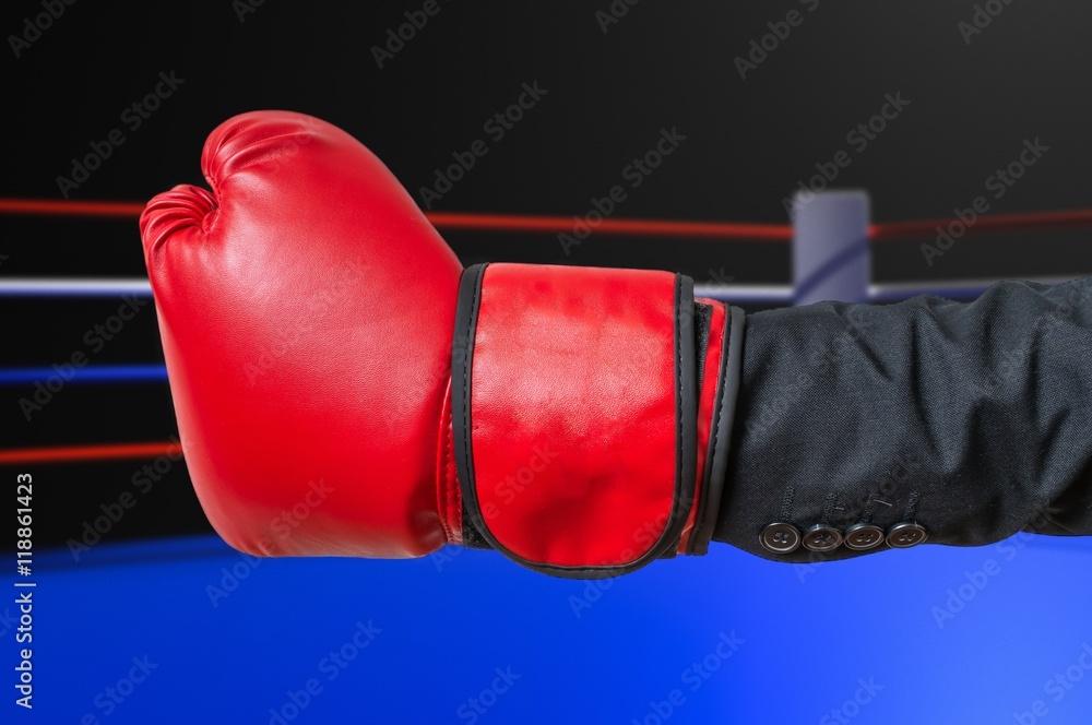 Hand of businessman in suit with red boxing glove in ring.