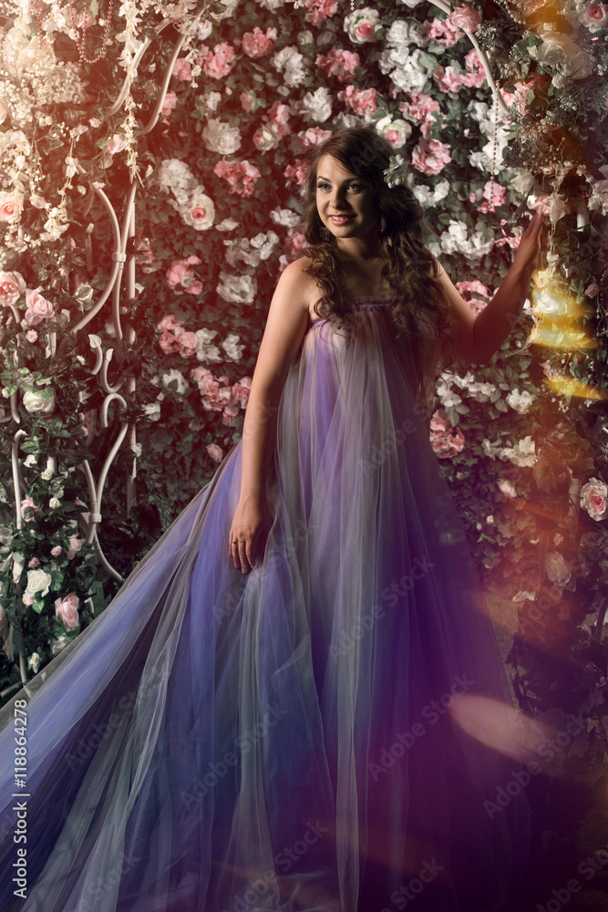 Beautiful woman standing in violet long dress under arch of pink and white roses