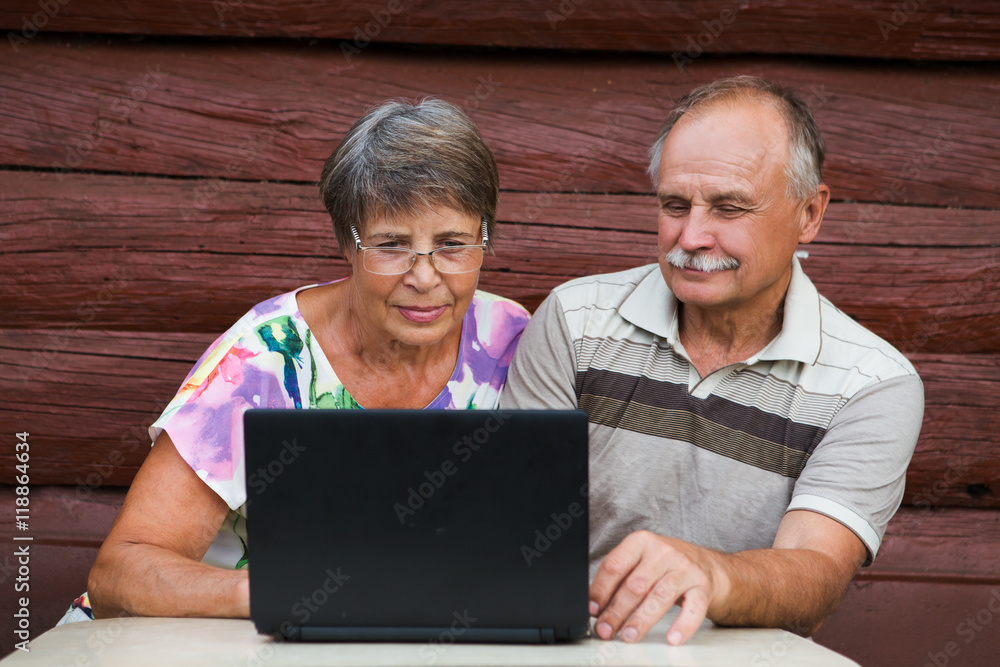 Elderly couple looking at their laptop on a wooden background of the house

