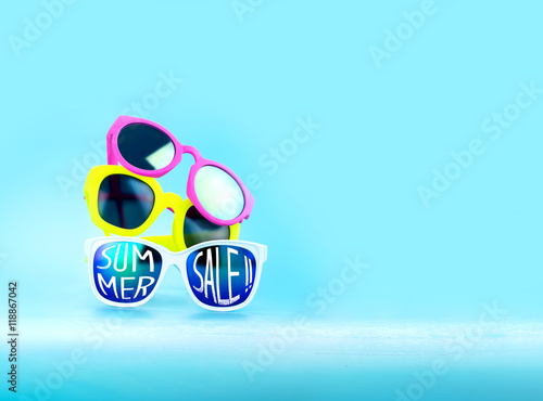 Stack of Sunglasses and summer sale word in light blue studio,S