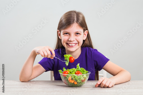 Happy little girl is eating salad.