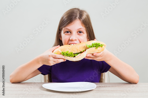 Little girl is eating sandwich for breakfast.