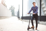 Pleasant smiling man riding a kick scooter