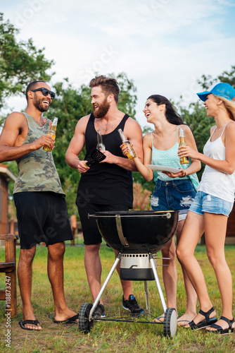 Friends drinking beer and frying meet on barbeque grill outdoors