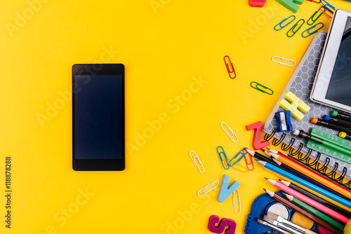 School supplies and mobile phone on yellow background