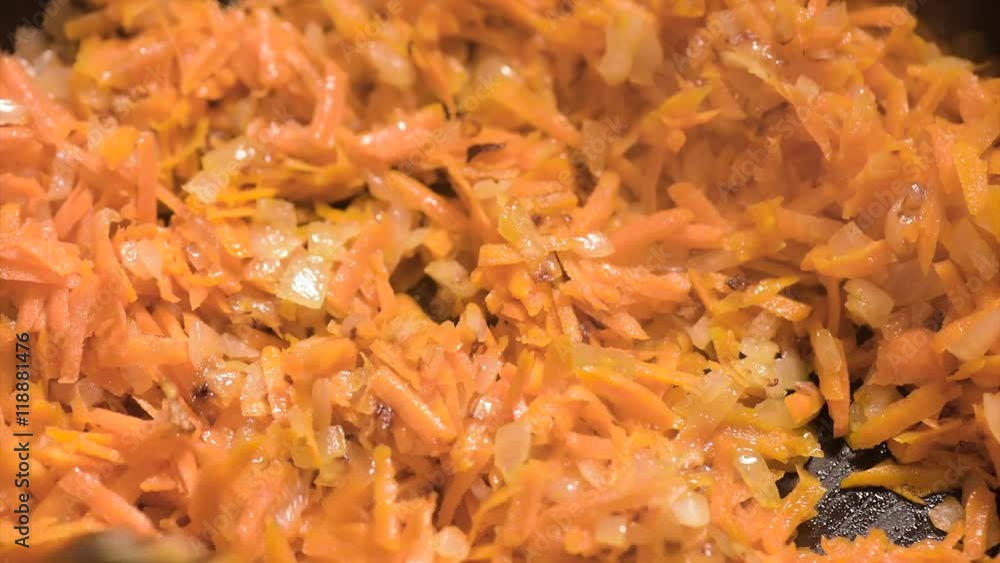 Chopped onions and carrots fried in vegetable oil in the pan. Close-up on top of a kitchen tile. Chopped onions and carrots fried in vegetable oil in the pan. Close-up on top of a kitchen tile.