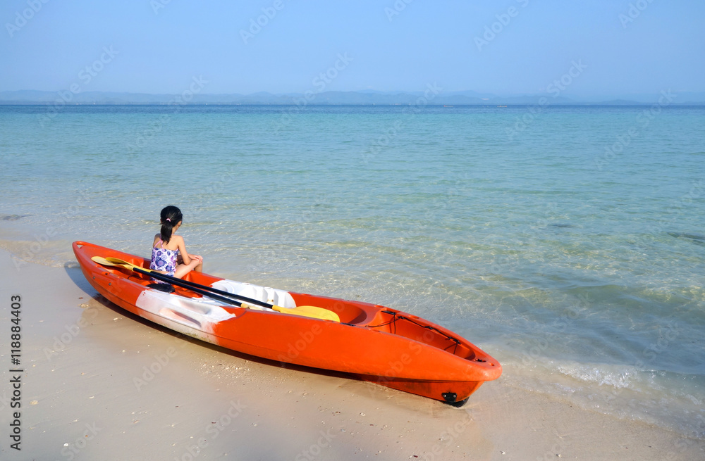 young asian girl in swimming suit sitting on orange kayak with yellow paddle on a sandy beach young asian girl in swimming suit sitting on orange kayak with yellow paddle on a sandy beach