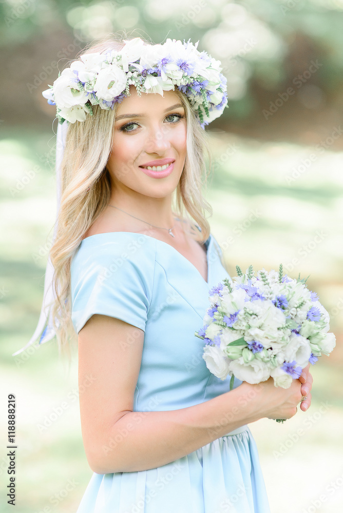 Lady in blue dress and white wreathe poses in green garden Lady in blue dress and white wreathe poses in green garden