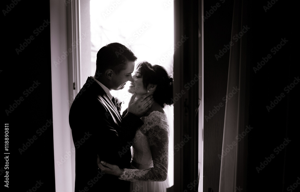 Groom holds bride's neck before a kiss while they stand in door
