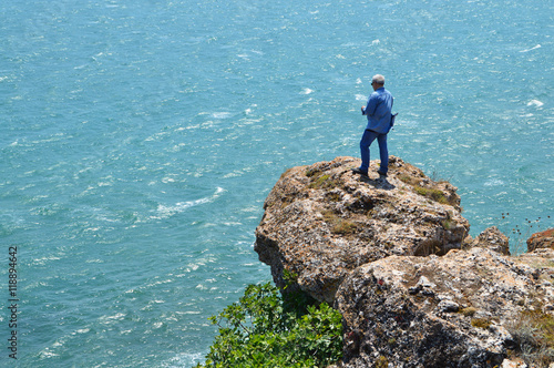 Gray haired man on a rock high above the blue sea