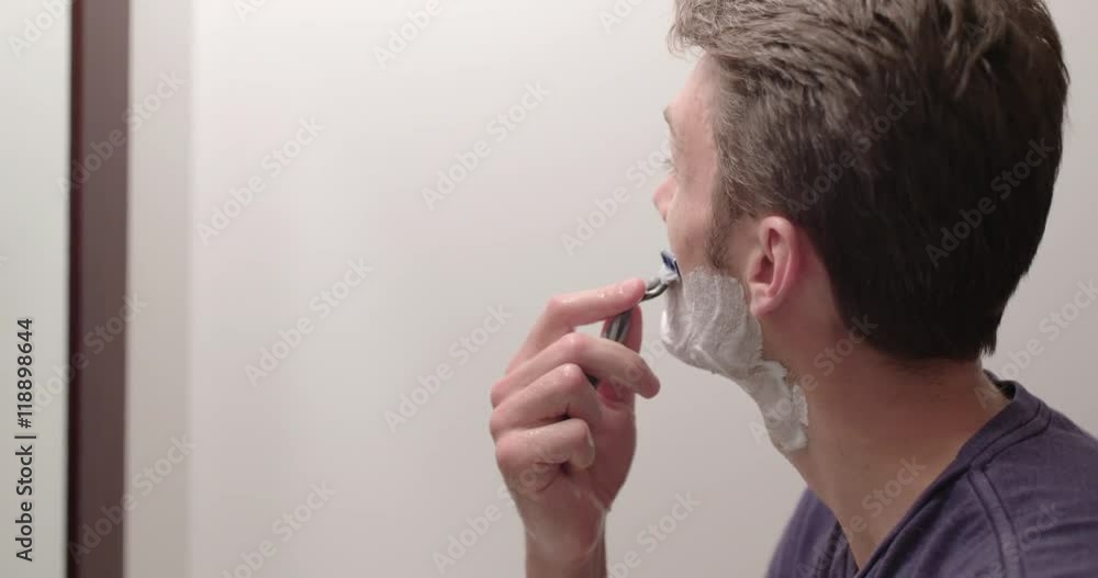 Man wet shaving to remove stubble while looking in a bathroom mirror. Slow motion recorded at 60fps, close up, profile. Man wet shaving to remove stubble while looking in a bathroom mirror. Slow motion recorded at 60fps, close up, profile.