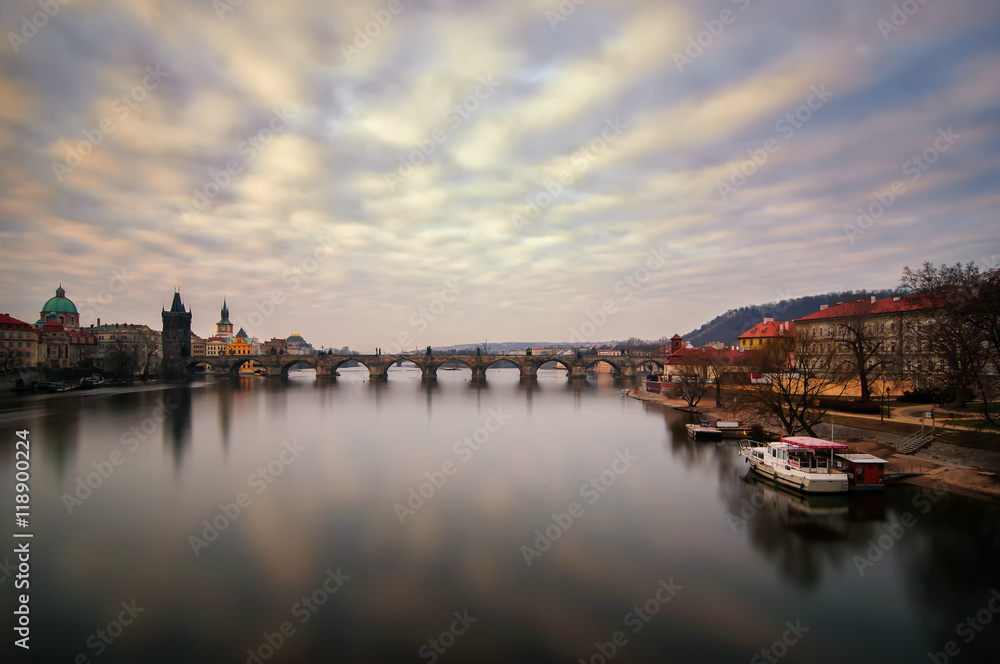 Beautiful sunrise near famous Charles Bridge with cloudy sky and water reflection. Bridge with amazing tower and old statues at early morning. Typical sunny day in Prague, Czech republic.