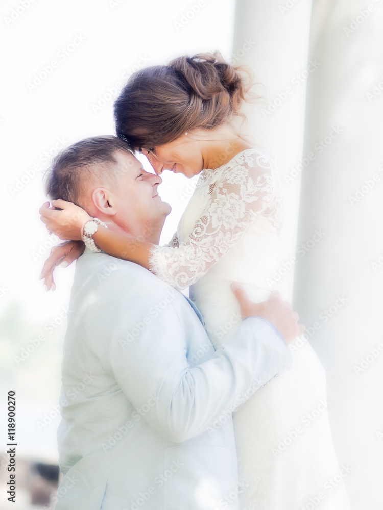 Groom embraces Russian bride on a background of white columns Groom embraces Russian bride on a background of white columns